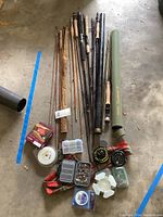 Full view of multiple bamboo and modern fly fishing rods, reels, several rod cases, fishing flies containers, and fishing accessories laid on the floor