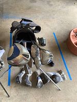 Overview of golf clubs arranged in front of golf bag on garage floor. Visible wood and iron clubs with covers nearby.