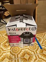 Instant Pot Duo Nova 3 Quart box closed on floor showing front branding and model info.