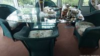 Overview of four wicker chairs around oval glass-top table with assorted decorative items on top.