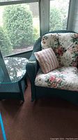View of green wicker rocker with floral cushions and matching glass-top side table