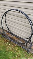 Photo of full metal rounded log holder leaning against beige siding outdoors giving overall view of item shape, size, and color.
