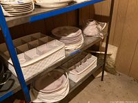 Shelf view showing stacks of dinner plates and coffee cups in two different floral patterns, along with a teapot wrapped in plastic.