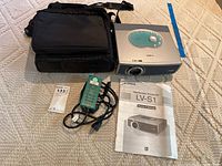 Canon LV-S1 multimedia projector with black carrying case, power cord, green accessory, and owner's manual.