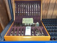 Full set of flatware in wood case showing knives, forks, spoons with patterned handles and case interior