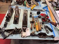 Overview of all woodworking tools including five Stanley hand planers, lathe chisels, hand drills, marking gauge, and spokeshave arranged on work table.