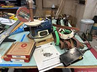 Overall view of Rikon belt and disc sander with sanding belts, discs, foot pedal and manual on table in basement workshop