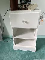 Front view of white side table showing drawer with clear knob and open shelf space below with adjustable shelf.