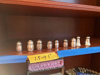 Nine sterling silver shakers lined up on a wooden shelf with a label indicating 1 to 1.5 inches tall.