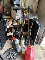 Full view of open black cabinet with assorted vehicle care tools and liquids, including large plastic bottles, hand tools, and hardware scattered on the floor and inside the cabinet.