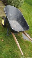 Overall view of black plastic wheelbarrow tub, wooden handles, and one air-filled tire showing wear and usage marks.