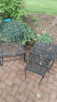 Metal bouncer chair and three metal nesting tables placed on brick patio near plants. Visible rust and outdoor dirt on all items.