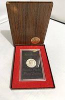 1972-S Eisenhower Proof Dollar coin encased in plastic with black card backing, placed inside original wood-patterned box with red felt interior and gold medallion on lid.