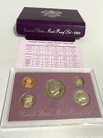 1988-S US Mint Proof Set in clear plastic holder with purple background, showing five coins and specification card below, with purple titled sleeve behind