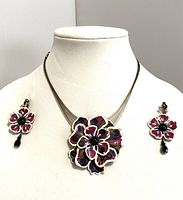 Full view of multi-strand necklace with large flower pendant and matching flower clip earrings on display stand.