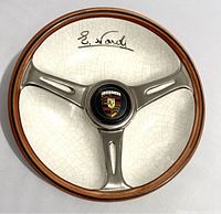 Top view of round ceramic ashtray displaying three-spoke steering wheel design, Porsche shield and E. Nardi signature