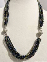 Front view of the multi-strand iridescent bead necklace showing the twisted strands and one magnetic clasp with filigree detail.