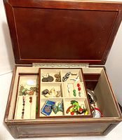 Top view of wooden jewelry box open showing two removable upper drawers with multiple compartments filled with assorted earrings, rings, pendants, and small jewelry items.