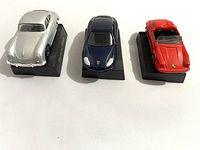 Front and top view of the silver, black, and red Porsche model cars on black plastic stands, showing color, size, and details of each car.