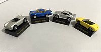 Four Maisto Porsche model cars on labeled black plastic stands arranged in a row, showing overall set condition and variety of models.