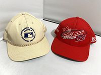 Front view of two baseball caps. The red cap is embroidered with 'HOME RUN RECORD 62' and signature. The beige cap features 'Professional Baseball Scouts of Northern California' and MLB logo.