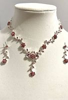 Overall view of necklace and earrings displayed on white bust mannequin showing floral pink rhinestone design with leaf details.