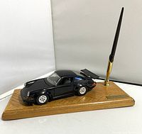 Side view of black Porsche 911 model attached to wooden base with pen holder and pen