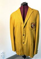 Front view of the gold colored Porsche suit jacket with emblem patch on the left chest pocket, jacket displayed on mannequin.
