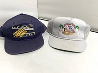 Two caps displayed from front: gray cap with embroidered Desert Storm logo and '91, blue cap with yellow printed Desert Storm logo and star accents.