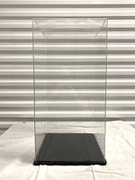 Front view of the tall rectangular acrylic display case on black plastic base with rubber feet.