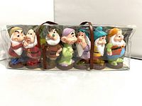 Seven vintage Disney Seven Dwarfs figurines lined up inside a clear plastic carrying case with brown straps, showing all characters side by side.