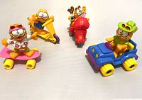 Photo showing a group of four Garfield figures each associated with a colorful vehicle: skateboard, scooter, jeep, and motorcycle