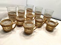 Front angled view showing six iced tea glasses and six coffee cups, all with glass bodies and woven wicker bases and handles.