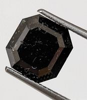 Octagon faceted black diamond held in tweezers, showing table and step facets