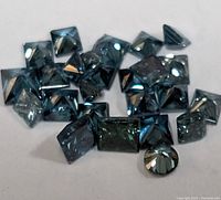 Close-up photo of multiple blue diamonds with princess and round cuts, positioned on white background.