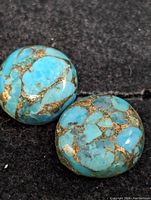 Two polished turquoise gemstones shown on black fabric background, highlighting their blue color and brown matrix pattern.