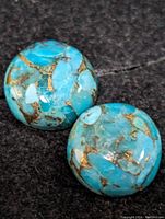 Pair of round turquoise gemstones on black background showing natural brown matrix pattern and bright blue color.