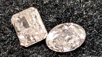 Two loose pink diamonds, square and oval cuts, displayed on a black fabric background, showing facets and color.