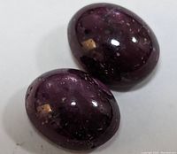 Two polished star ruby gemstones showing deep reddish-purple color and natural inclusions, laid side by side on white background.
