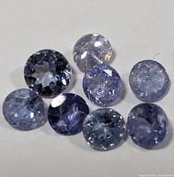 Eight loose round faceted tanzanite gemstones laid on a flat surface showing color and cut details.