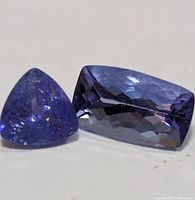 Clear close-up of two faceted tanzanite gemstones showing color and cut details, triangular and rectangular shapes.