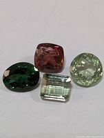 Four cut and polished tourmaline gemstones of varying shapes and colors laid out on a white surface.