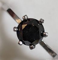 Close-up of the black diamond atop the silver ring, showing the six-prong setting and facets of the stone.