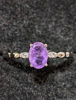 Close-up photo of sterling silver ring with oval purple amethyst stone and small clear accent stones on band, on black background.