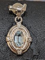 Close-up of front of sterling silver aquamarine pendant showing oval cut blue gemstone and small clear stone accents on silver setting