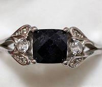 Close-up front view showing faceted black onyx center cushion-cut stone with two clear round stones set in ornate sterling silver band.