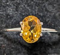 Close-up image of sterling silver ring with faceted oval citrine gemstone on a dark fabric background.