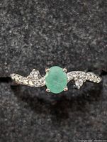 Close-up frontal view of the sterling silver ring with oval emerald center and diamond accents on band.