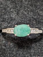 Front view of sterling silver ring with oval-shaped green emerald center stone and small clear stones on the band.
