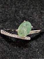 Close-up photo of the sterling silver ring showing the oval emerald held by four prongs with small round clear stones along the band.